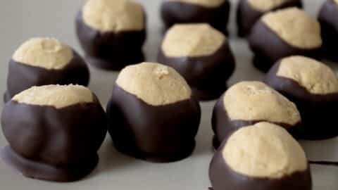 Several buckeye candies, made with the Easy Buckeyes Recipe, feature creamy peanut butter centers partially dipped in chocolate and are arranged on a light-colored plate.
