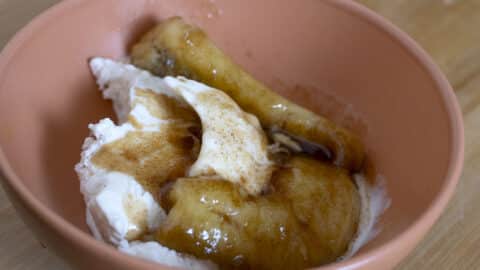 A peach-colored bowl with vanilla ice cream topped with caramelized bananas and brown syrup on a wooden surface, inspired by a classic Bananas Foster recipe.