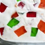 Close-up of a dessert featuring red, green, and orange gelatin cubes suspended in a creamy white mixture, likely set in a glass dish—perfect for showcasing a classic Broken Glass Cake Recipe.