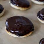 Close-up of round cookies with a shiny, thick layer of chocolate icing on top, arranged on parchment paper—perfect for anyone craving an authentic Berger Cookies Recipe treat.