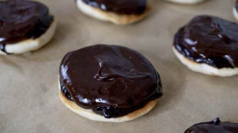 Close-up of round cookies with a shiny, thick layer of chocolate icing on top, arranged on parchment paper—perfect for anyone craving an authentic Berger Cookies Recipe treat.