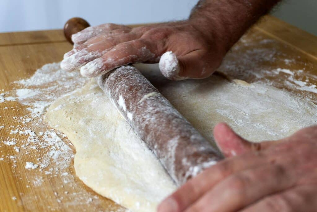 Dough being rolled out by a rolling pin on a table for Dollywood Cinnamon Bread.
