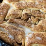 Close-up of freshly baked cinnamon rolls in a skillet, topped with a drizzle of melted icing, showcasing their golden-brown, fluffy texture—reminiscent of the famous Dollywood Cinnamon Bread Recipe.