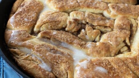 Close-up of freshly baked cinnamon rolls in a skillet, topped with a drizzle of melted icing, showcasing their golden-brown, fluffy texture—reminiscent of the famous Dollywood Cinnamon Bread Recipe.