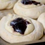 Round pastries with a light golden crust, each topped with a dollop of creamy filling and a generous portion of dark red fruit jam, showcase the classic Texas Kolaches recipe on parchment paper.