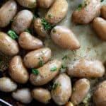 Small roasted salt potatoes with skins on, glistening with oil and sprinkled with chopped fresh herbs, spread out on a baking sheet.