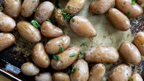 Small roasted salt potatoes with skins on, glistening with oil and sprinkled with chopped fresh herbs, spread out on a baking sheet.
