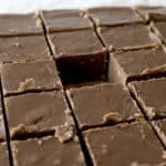 Close-up of chocolate fudge cut into squares, with one piece missing from the center, showing creamy texture and smooth tops—just like a classic Mackinac Island Fudge Recipe—on a parchment-lined surface.