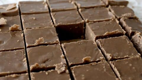 Close-up of chocolate fudge cut into squares, with one piece missing from the center, showing creamy texture and smooth tops—just like a classic Mackinac Island Fudge Recipe—on a parchment-lined surface.