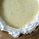 A classic Key lime pie in a glass dish features a graham cracker crust, creamy yellow filling, whipped cream piped around the edge, and a sprinkle of fresh lime zest on top.