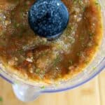A close-up, top-down view of a food processor containing freshly blended salsa with visible pieces of tomatoes, onions, garlic, and cilantro—perfect for making a delicious Salsa Tatemada Recipe. The processor rests on a wooden surface.