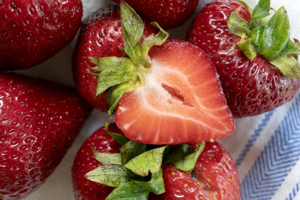 A group of strawberries on a rag with one cut in half on top.