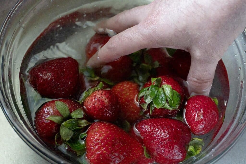 Strawberries being washed in water inside of a bowl.