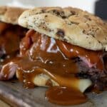 Two sandwiches on a tray, packed with North Shore Beef, melted cheese, and thick brown barbecue sauce, all served on poppy seed buns.