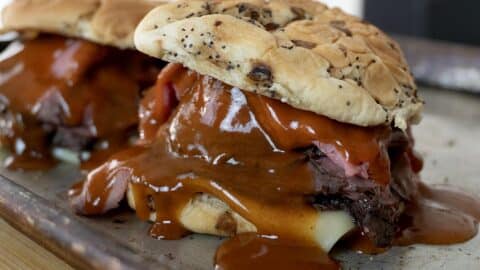 Two sandwiches on a tray, packed with North Shore Beef, melted cheese, and thick brown barbecue sauce, all served on poppy seed buns.