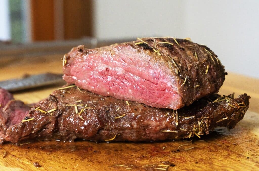 Smoked tri tip cut in half and sitting on a wooden cutting board.