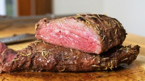 Smoked tri tip cut in half and sitting on a wooden cutting board.