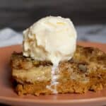A slice of pumpkin dump cake topped with a scoop of vanilla ice cream on a pink plate. The ice cream is slightly melting and dripping down the side of the cake, making this pumpkin dump cake recipe extra tempting.