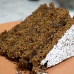 A close-up of a single slice of spiced Apple Stack Cake with a crumbly texture, topped with powdered sugar, resting on an orange plate.