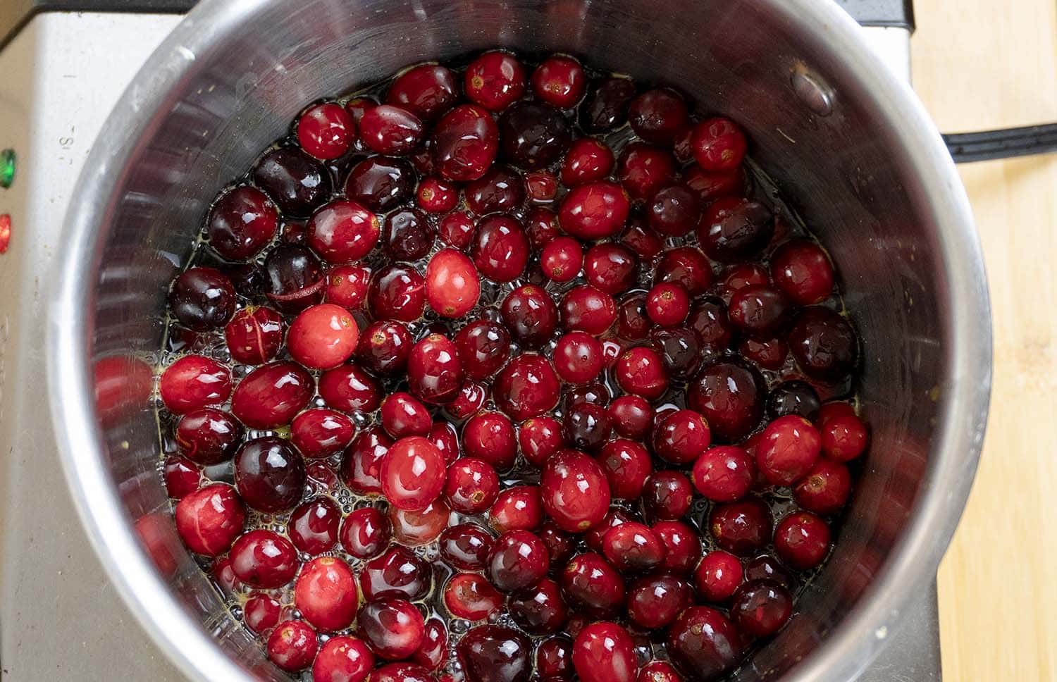 A pot filled with fresh cranberries cooking in liquid on a stovetop, preparing to make cranberry sauce.