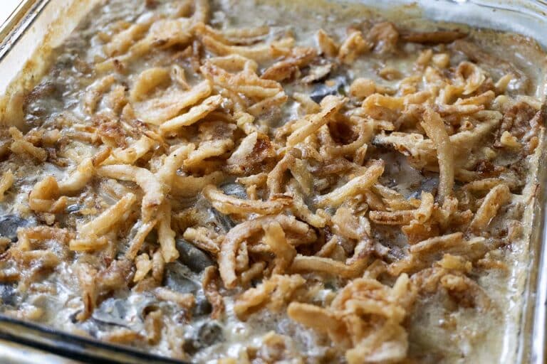 A close-up of a baked green bean casserole topped with crispy fried onions in a glass baking dish. The golden onions and creamy sauce are visible on the surface.