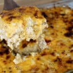 A serving of cheesy baked macaroni and cheese is lifted out of a glass baking dish, revealing a golden, bubbly, and slightly browned melted cheese topping.
