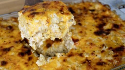 A serving of cheesy baked macaroni and cheese is lifted out of a glass baking dish, revealing a golden, bubbly, and slightly browned melted cheese topping.
