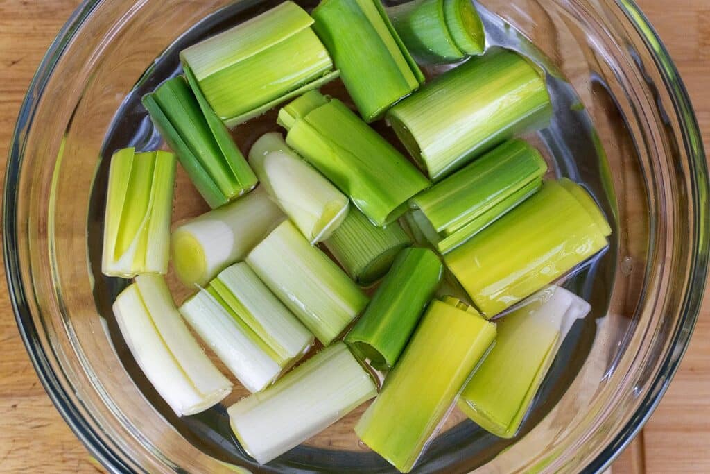Chopped pieces of leek soaking in a clear bowl of water, placed on a wooden surface.