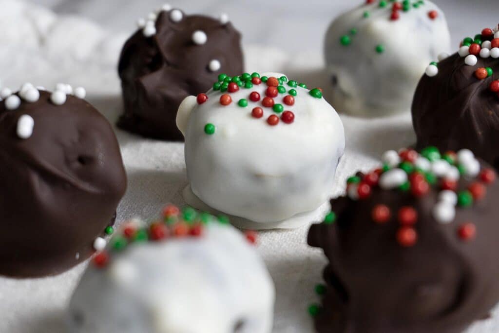 Close-up of chocolate truffles coated in white and dark chocolate, topped with festive red, green, and white sprinkles, arranged on a white surface.