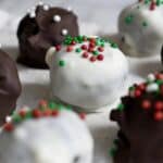 Close-up of chocolate truffles coated in white and dark chocolate, topped with festive red, green, and white sprinkles, arranged on a white surface.