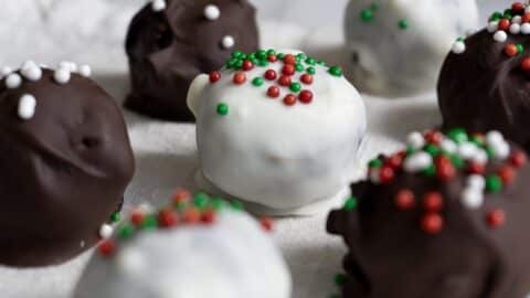 Close-up of chocolate truffles coated in white and dark chocolate, topped with festive red, green, and white sprinkles, arranged on a white surface.