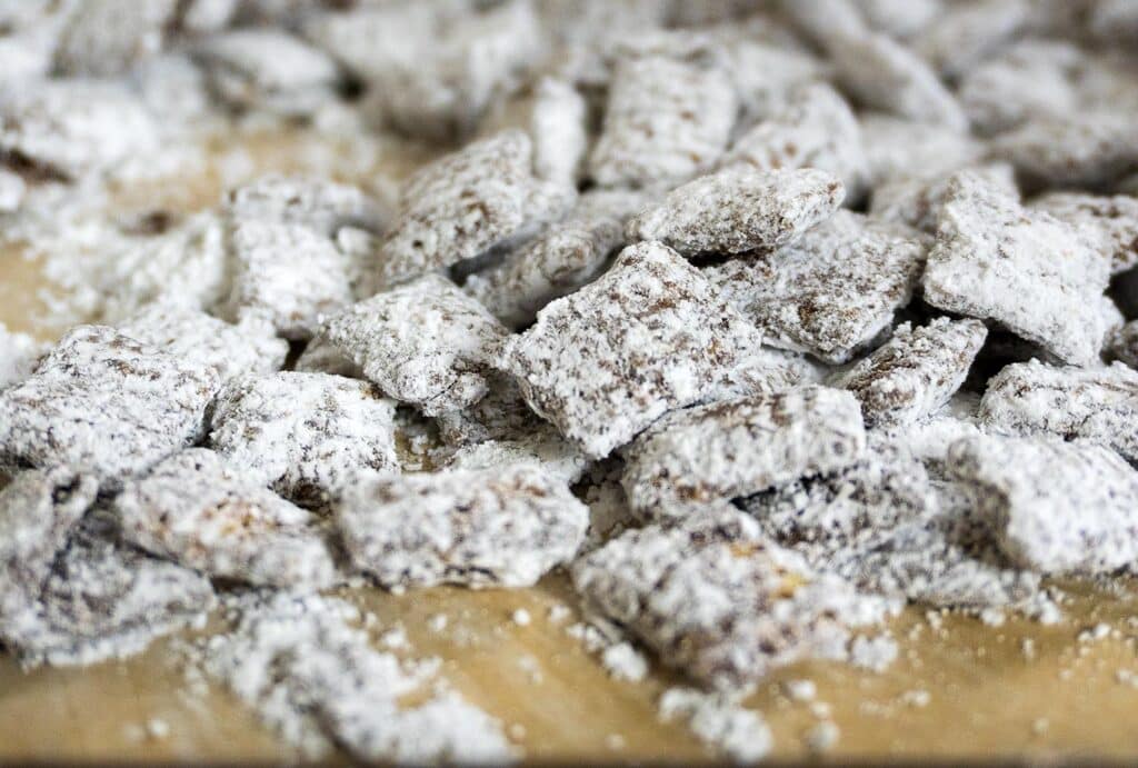A close-up of a pile of chocolate-covered cereal squares coated in powdered sugar, scattered on a wooden surface.