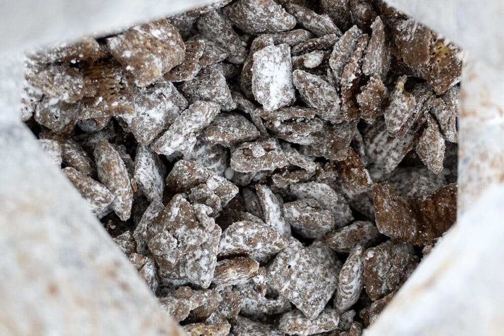 A close-up view of chocolate-coated cereal pieces dusted with powdered sugar, seen inside an open bag.