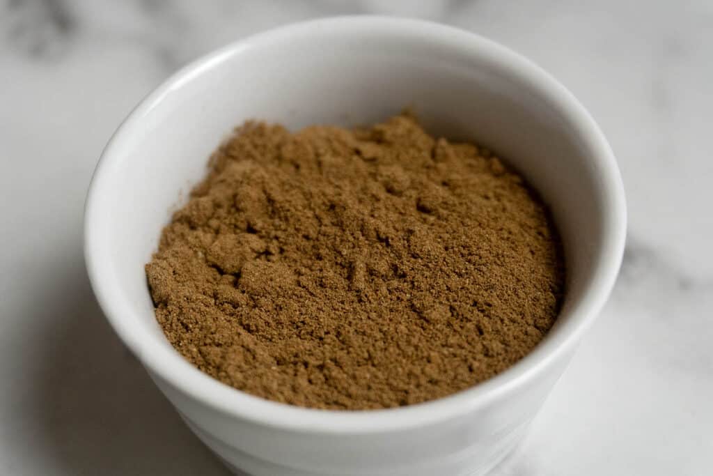 A white bowl filled with a fine, light brown powder sits on a white marble surface.