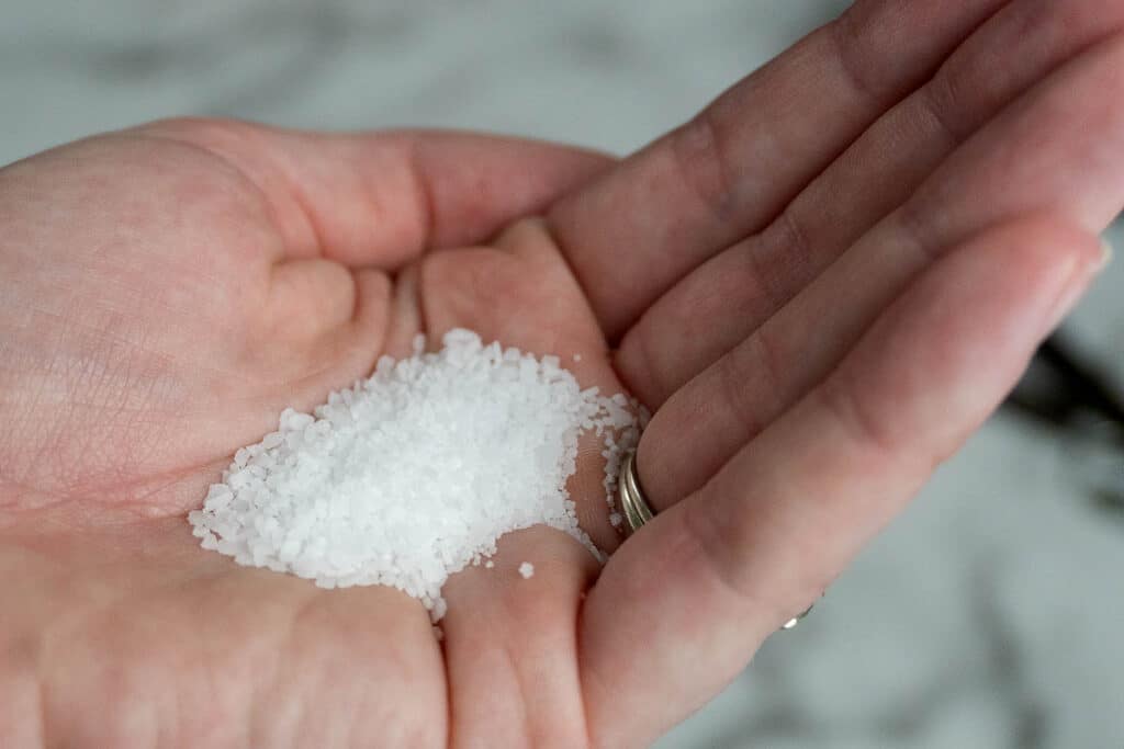 A close-up of a hand holding a small pile of coarse white salt crystals on the palm.