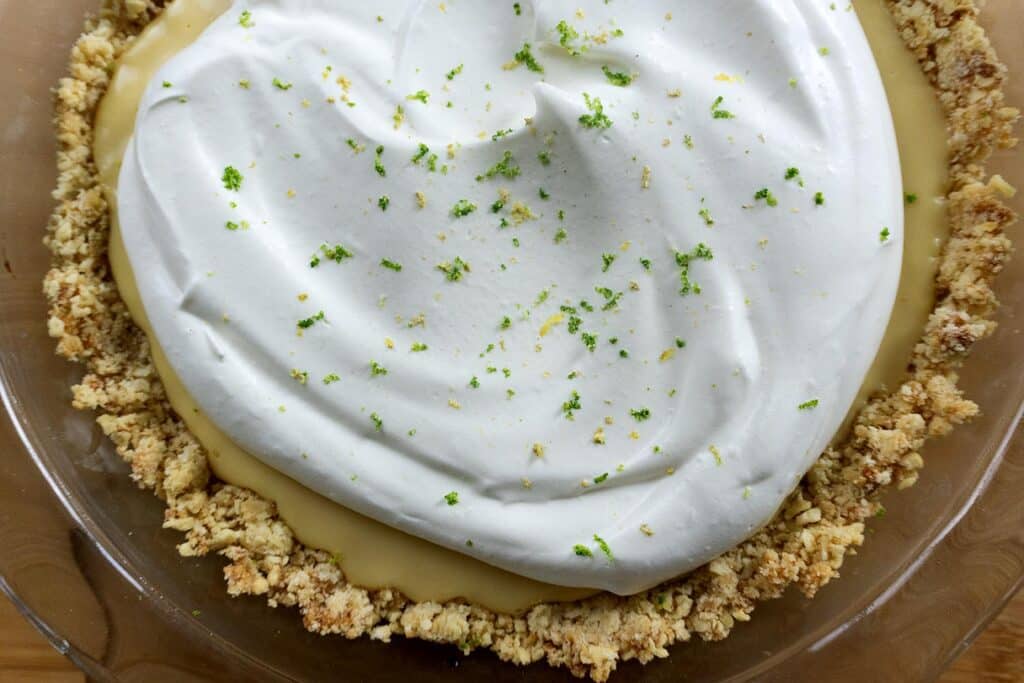 A homemade key lime pie with a crumbly crust, creamy yellow filling, and a fluffy layer of whipped cream on top, garnished with lime zest.