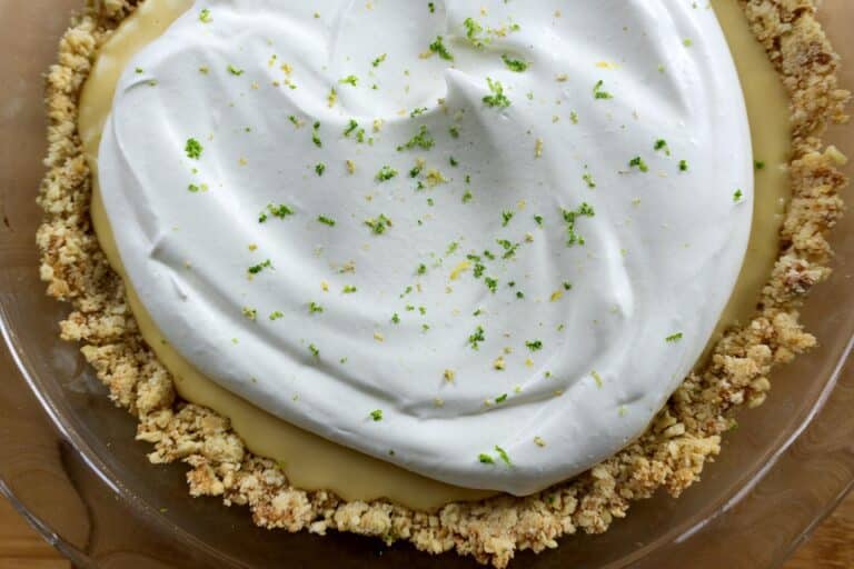 A homemade key lime pie with a crumbly crust, creamy yellow filling, and a fluffy layer of whipped cream on top, garnished with lime zest.