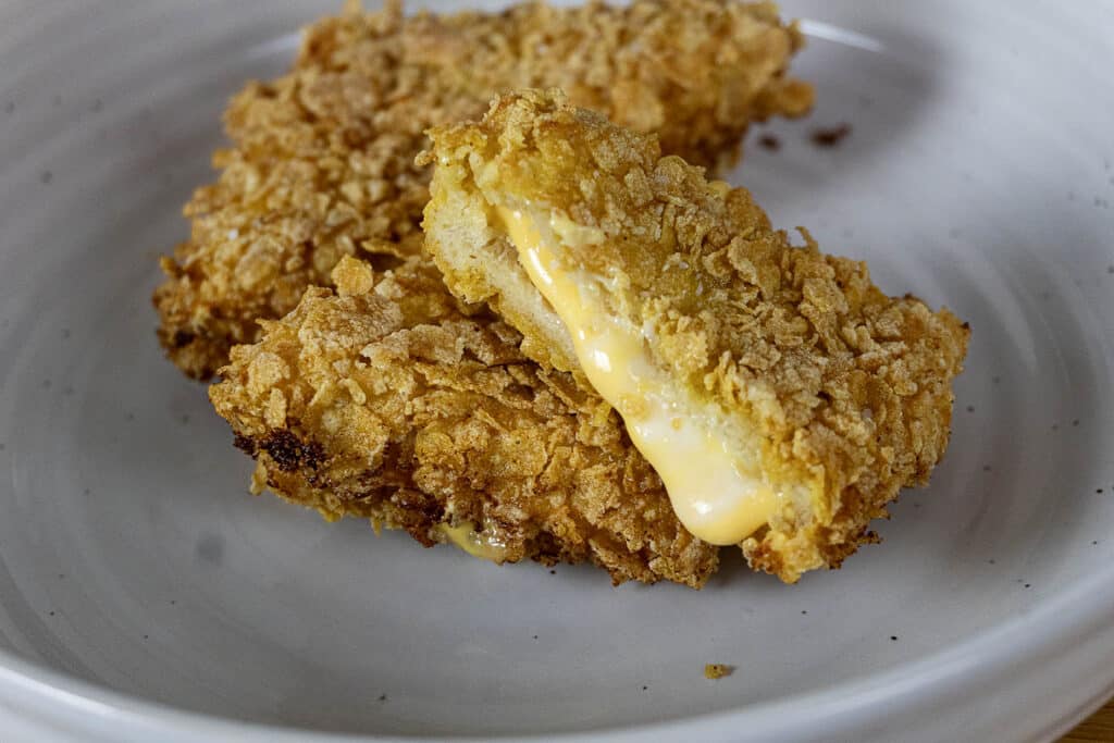 Two pieces of crispy, golden-brown fried food on a white plate; one is broken open to reveal melted cheese oozing out from the center.