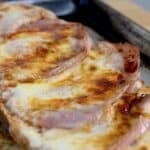 A close-up of a slice of a Gerber Sandwich topped with melted cheese and several strips of ham, resting on a metal baking sheet.