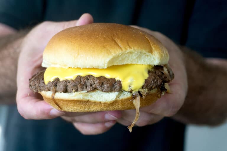 A person holds a cheeseburger with a beef patty, melted cheese, and a soft bun in both hands.