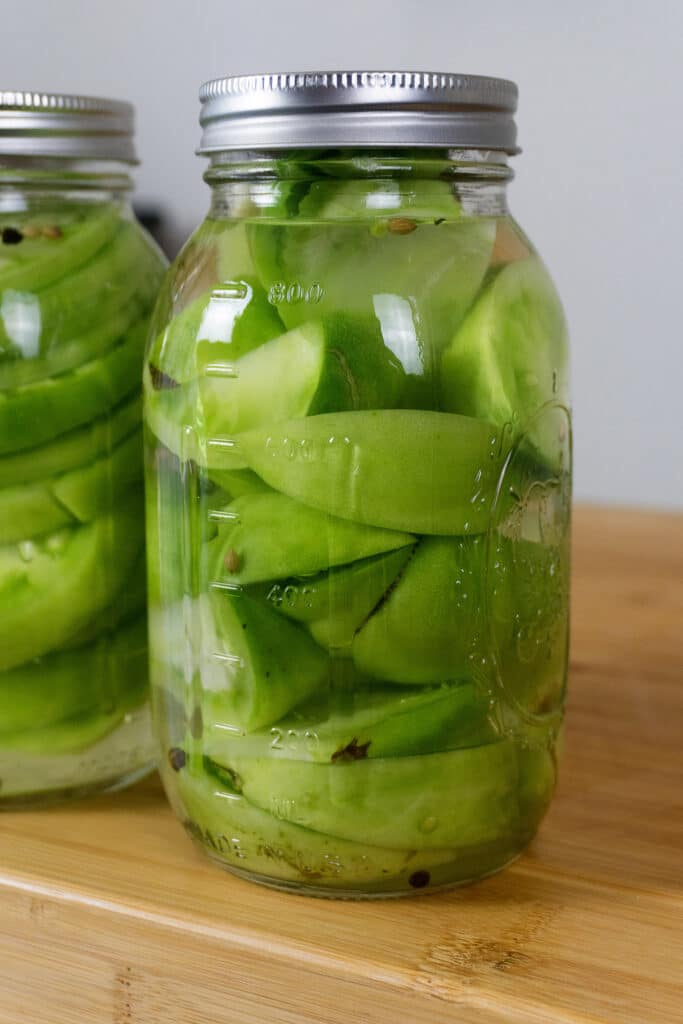 Two glass jars filled with sliced green apples submerged in liquid, sealed with metal lids, sitting on a wooden surface.