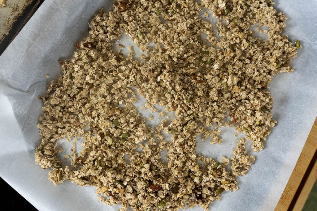 Unbaked granola mixture with oats and seeds spread on a parchment-lined baking sheet, ready to go into the oven.