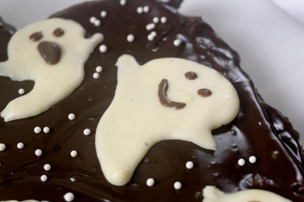 Chocolate-frosted brownie decorated with white chocolate ghosts and small white sprinkles.