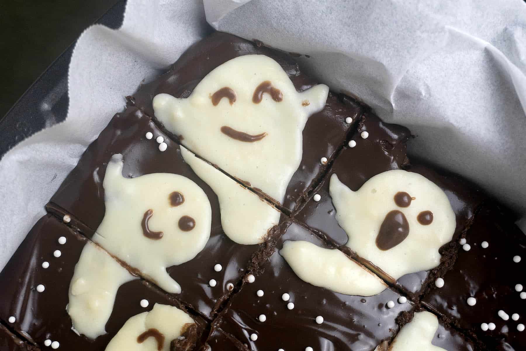 A pan of chocolate brownies decorated with white icing ghosts and small white sprinkles.