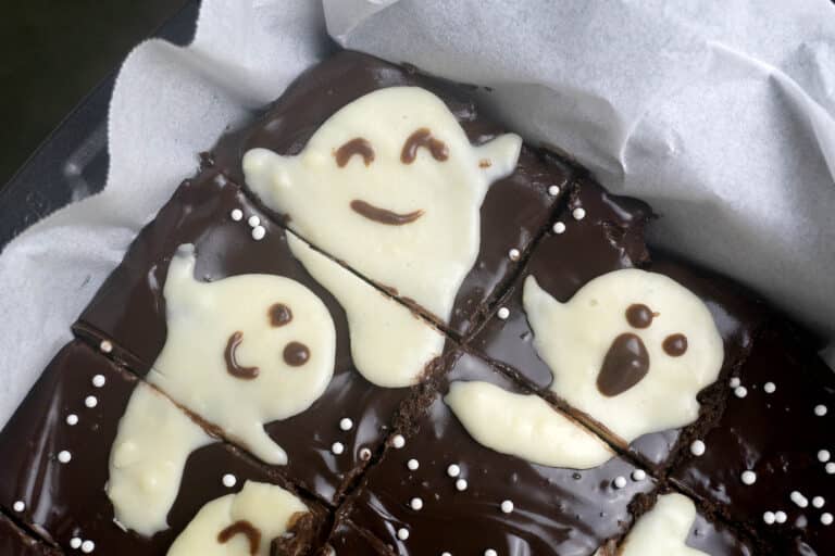 Chocolate brownies topped with white icing shaped like ghosts and sprinkled with white nonpareils.