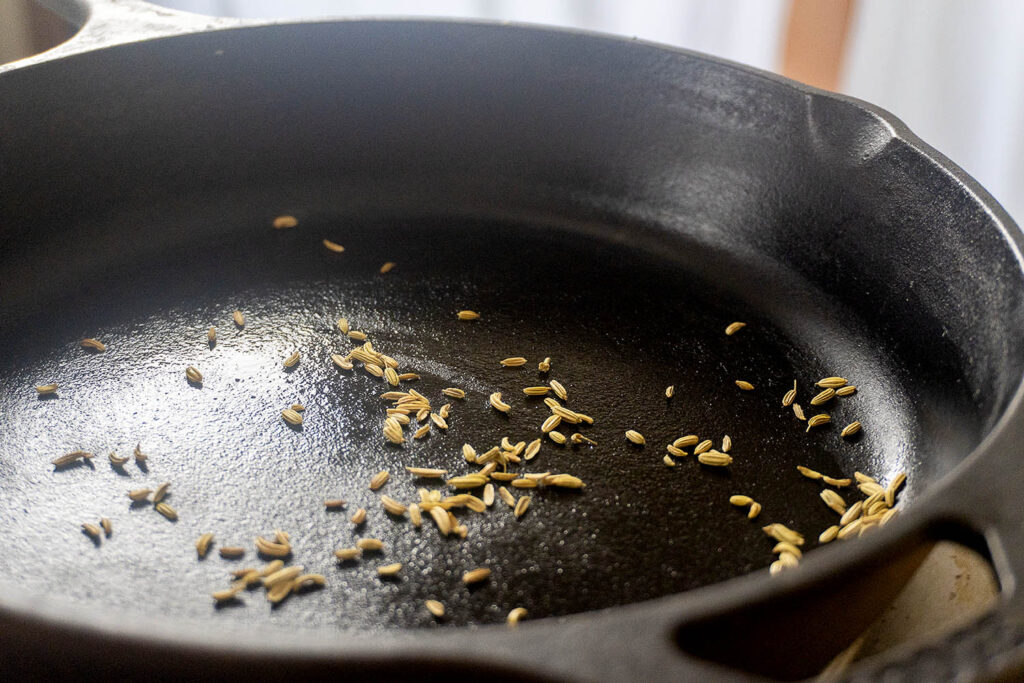 Fennel seeds scattered in a cast iron skillet.