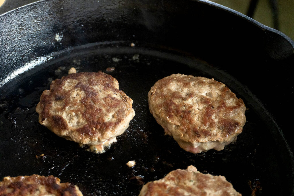 Three brown sausage patties frying in a cast iron skillet.