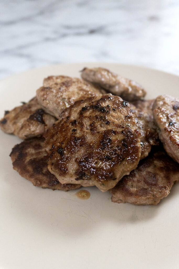 A plate piled with several cooked, browned sausage patties.